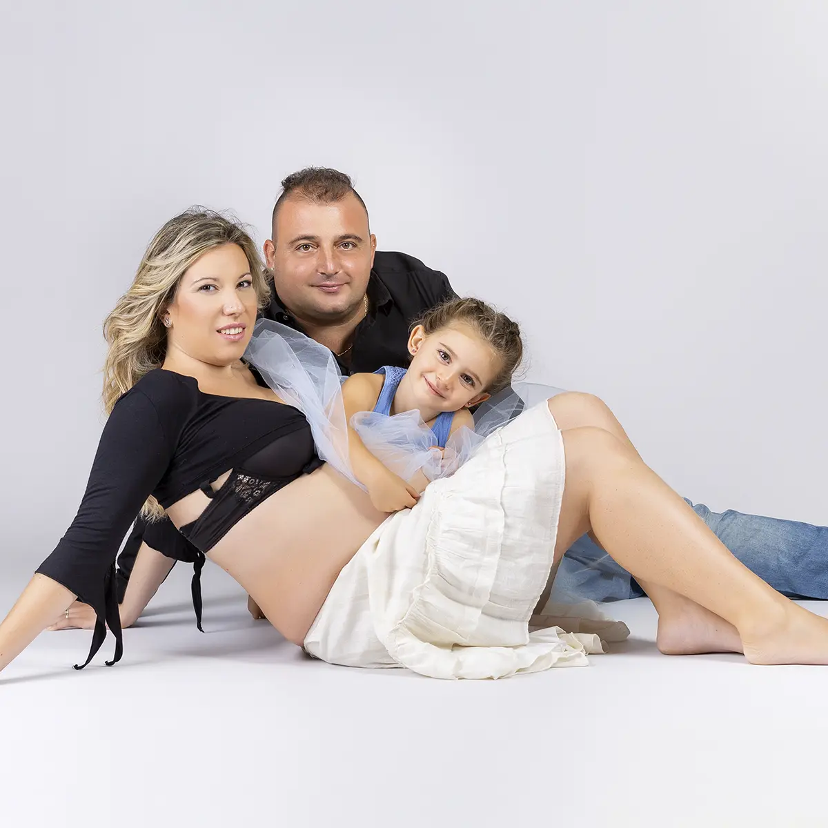 Famiglia in attesa con la figlia maggiore che abbraccia il pancione durante un book fotografico gravidanza in studio a Milano
