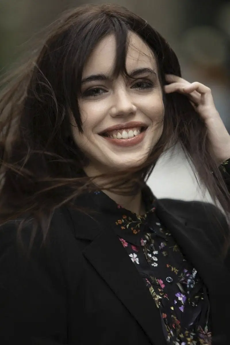 Sorriso naturale e occhi coinvolti in un ritratto femminile all'aperto, con movimento nei capelli