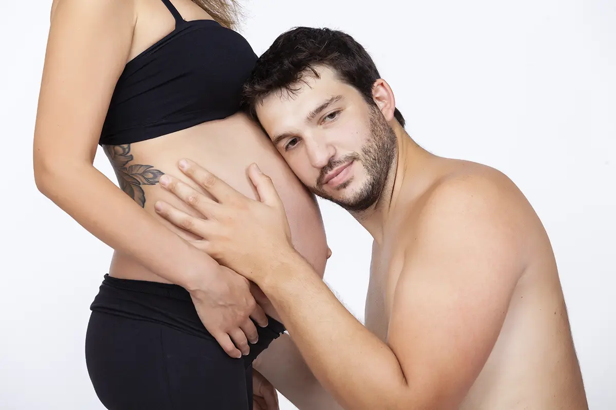 Futuro papà che bacia il pancione della compagna durante un book fotografico gravidanza in studio a Milano